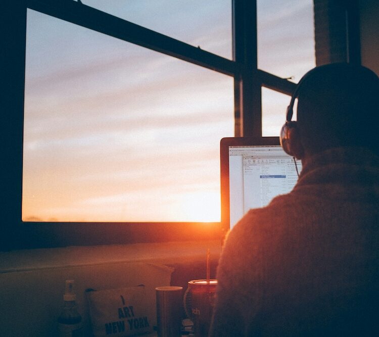 view of man's back of head looking at his laptop with a sunrise